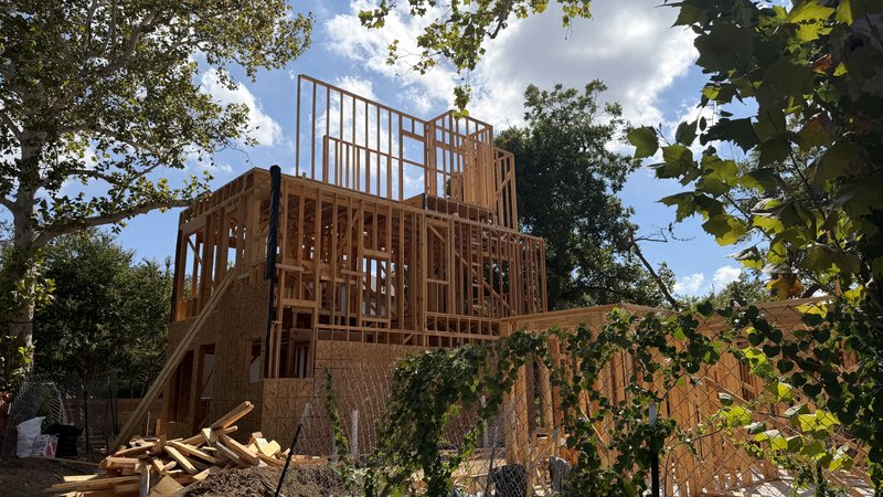 The sheathed three-story frame of Home 1 from the fence line